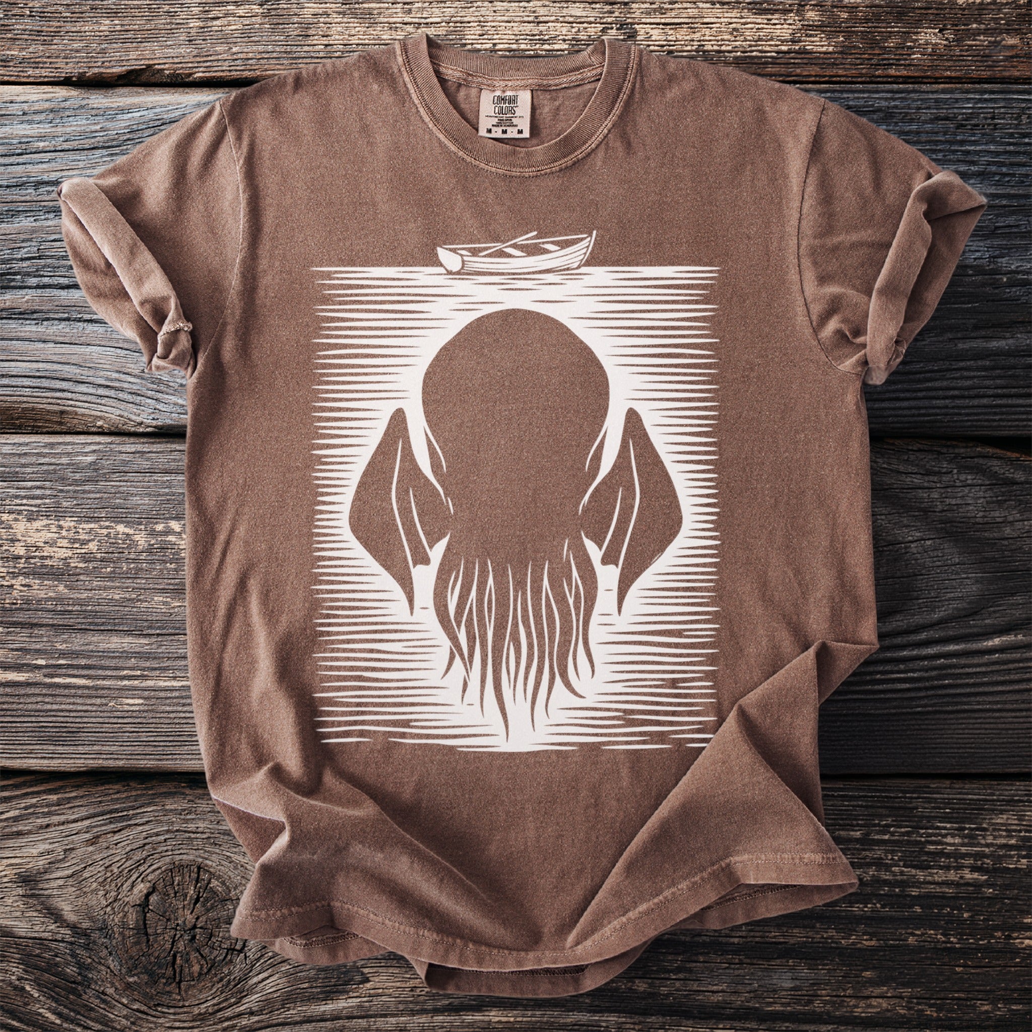 Brown t-shirt with a white linocut print of a tentacled creature and a boat.