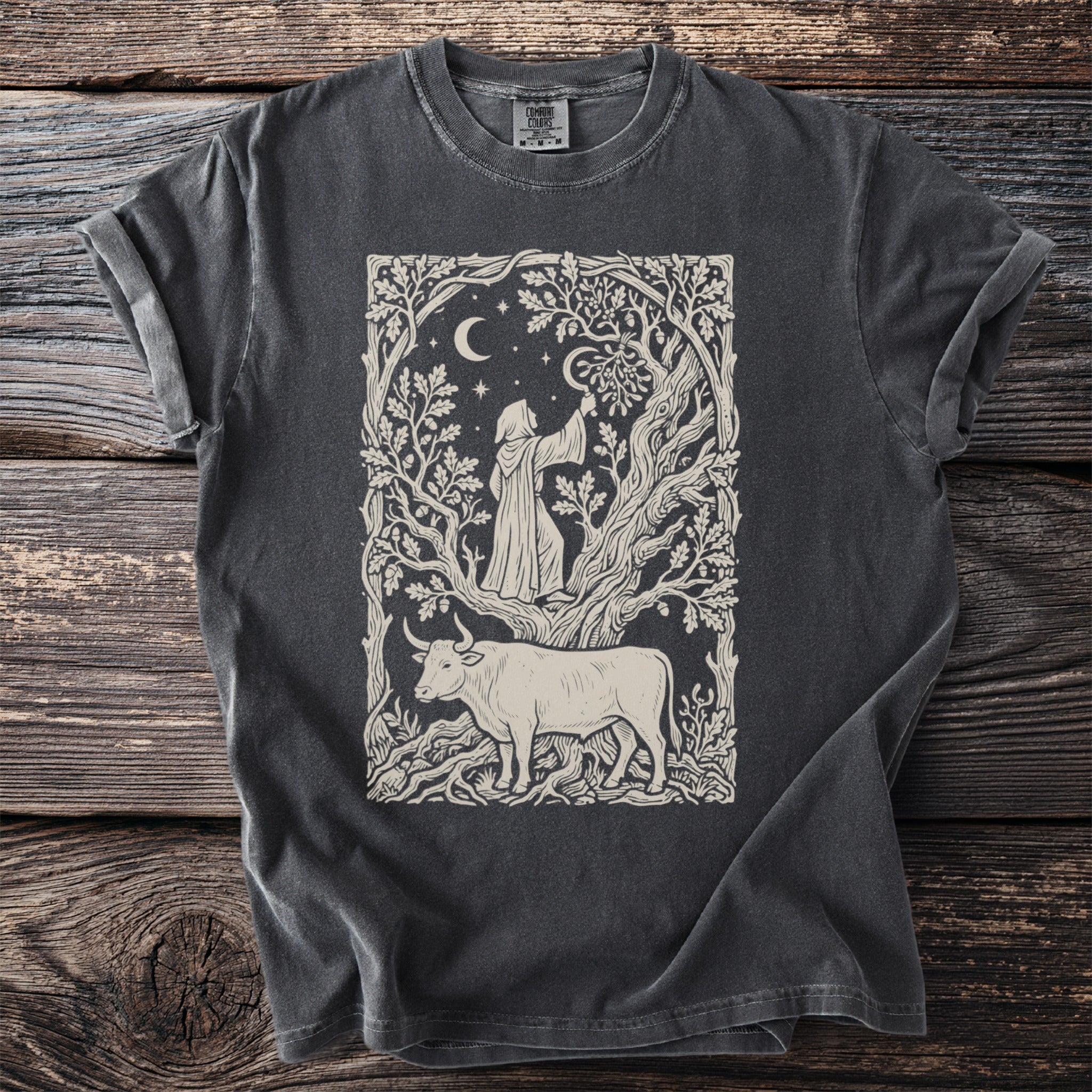 Dark t-shirt featuring a medieval-style print of a bull and a robed figure in a forest scene under the moon and stars.