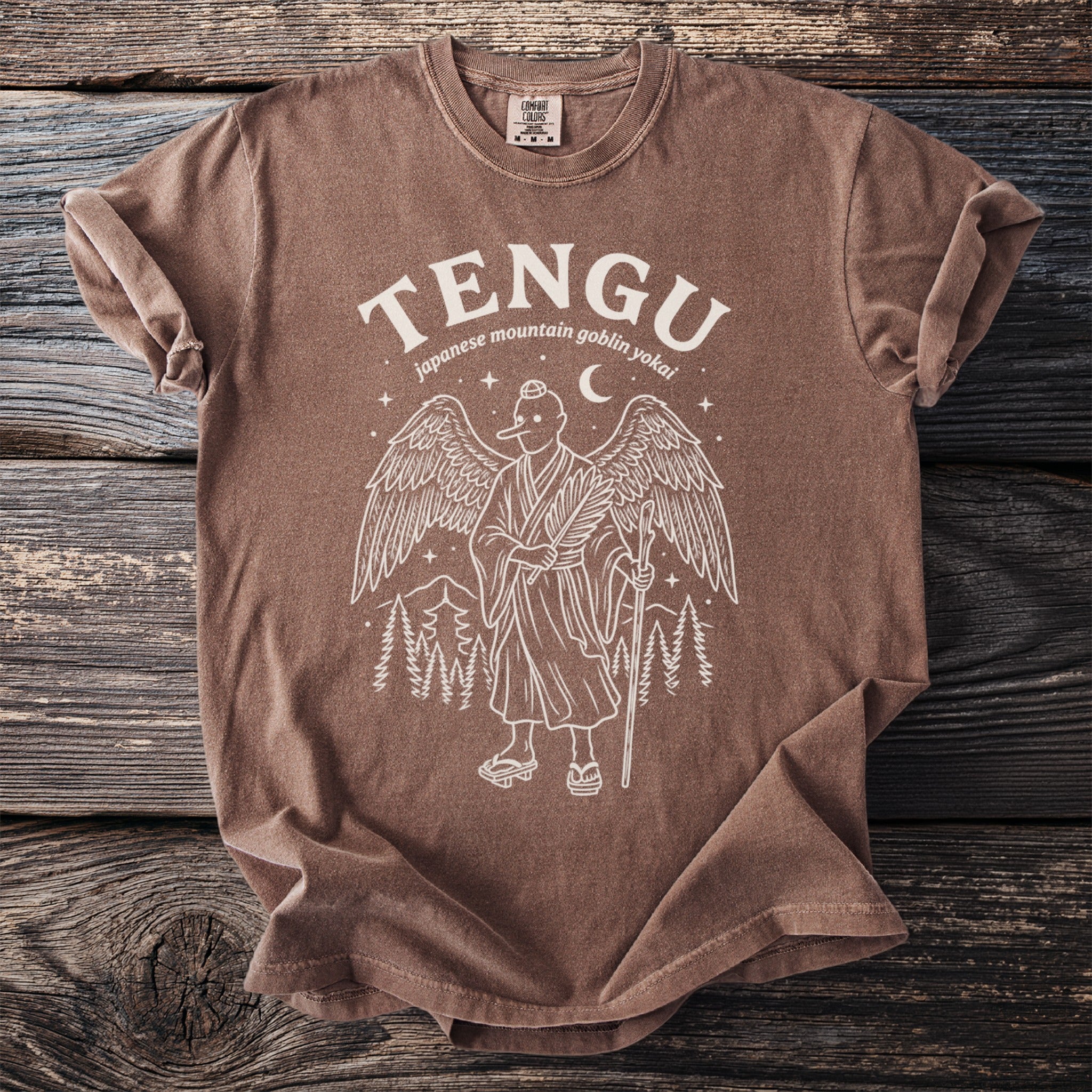 Brown t-shirt with white graphic of a Tengu with wings, holding a staff and fan.