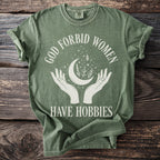 Green t-shirt with white text and graphics featuring 'God forbid women have hobbies'.