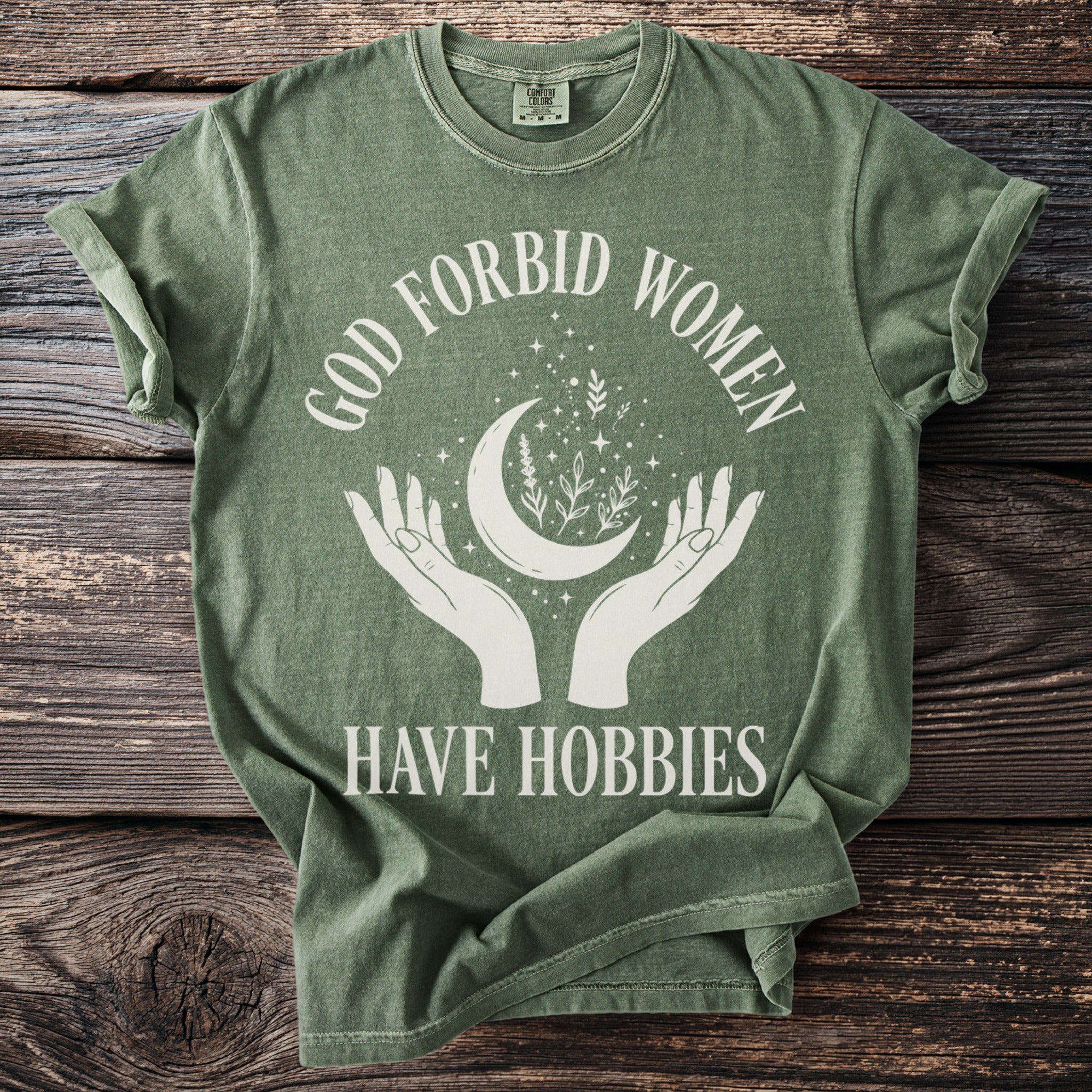 Green t-shirt with white text and graphics featuring 'God forbid women have hobbies'.