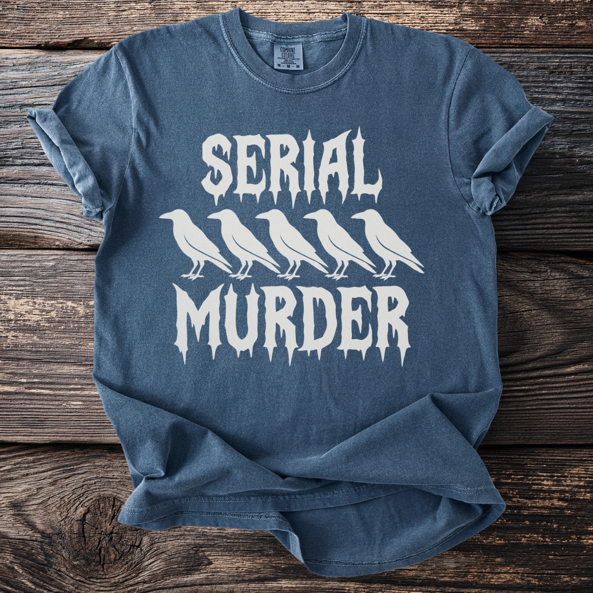 Blue t-shirt with white text "SERIAL MURDER" and a row of ravens.