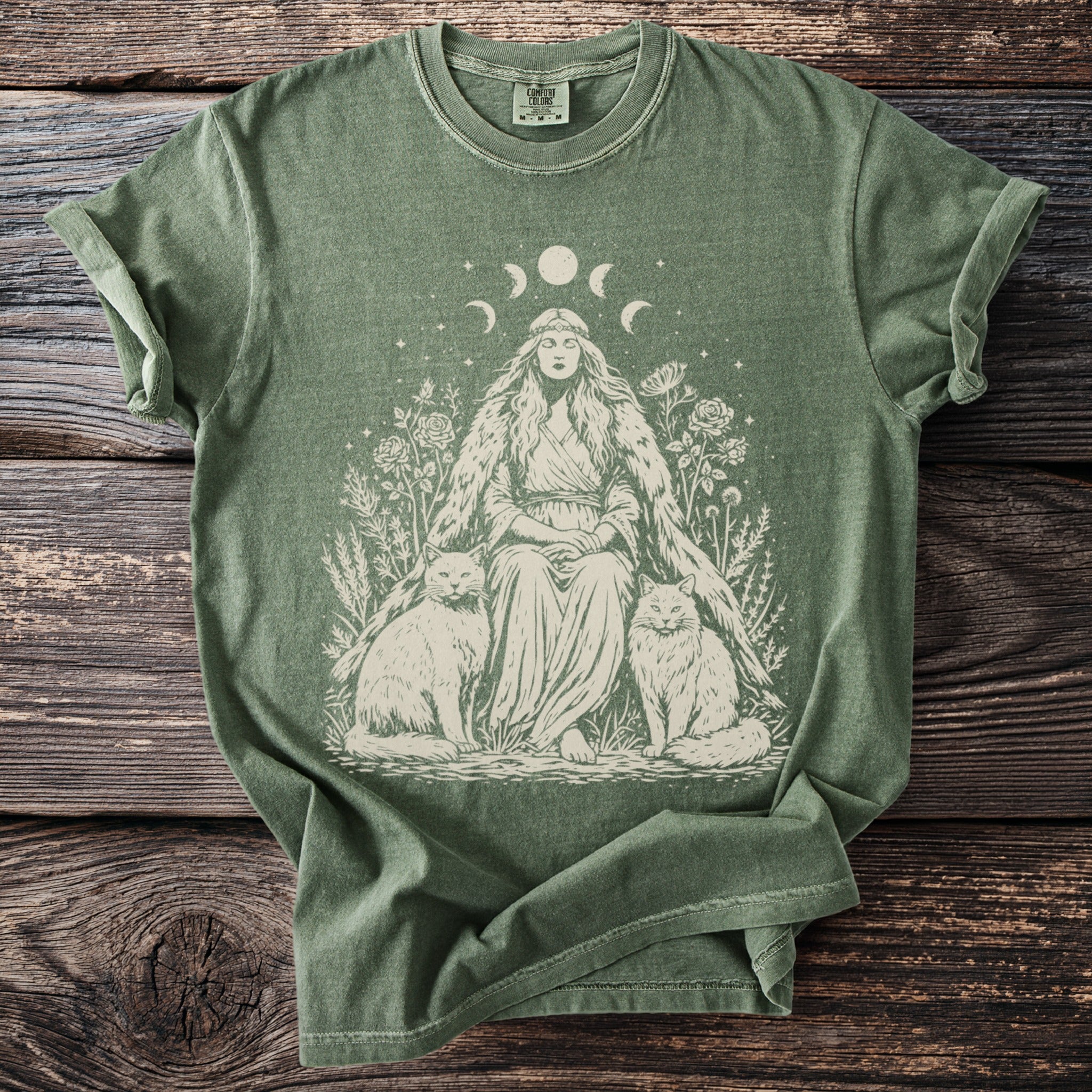 Green t-shirt with a woman, moon phases, flowers, and two cats in a line drawing.