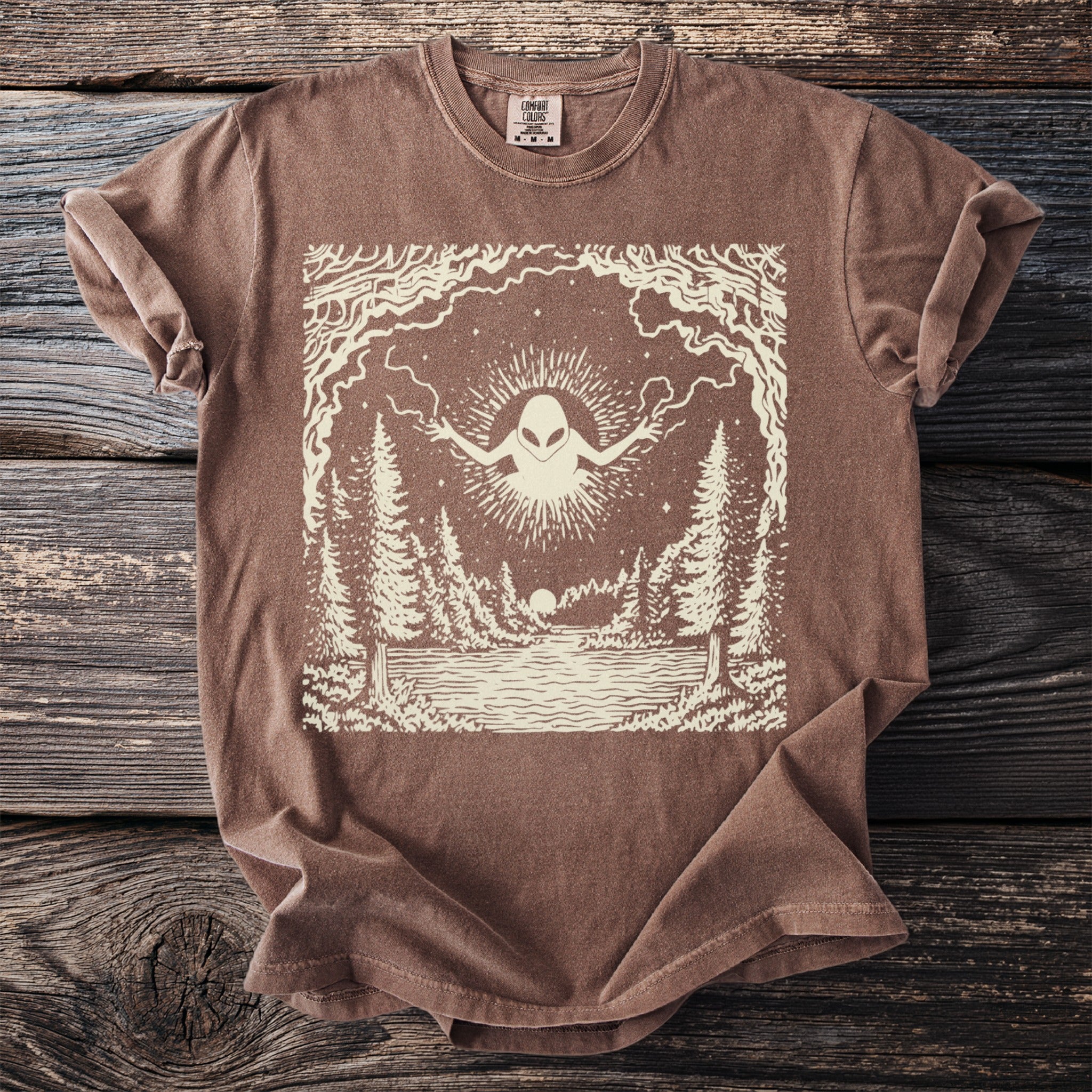 T-shirt with an alien design over a forest and lake scene.