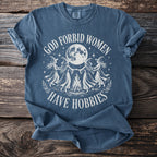 Blue t-shirt with white graphic of four witches dancing around a campfire under a full moon.