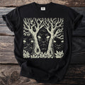Black t-shirt with a cream linocut print of three faces within trees on a starry background.