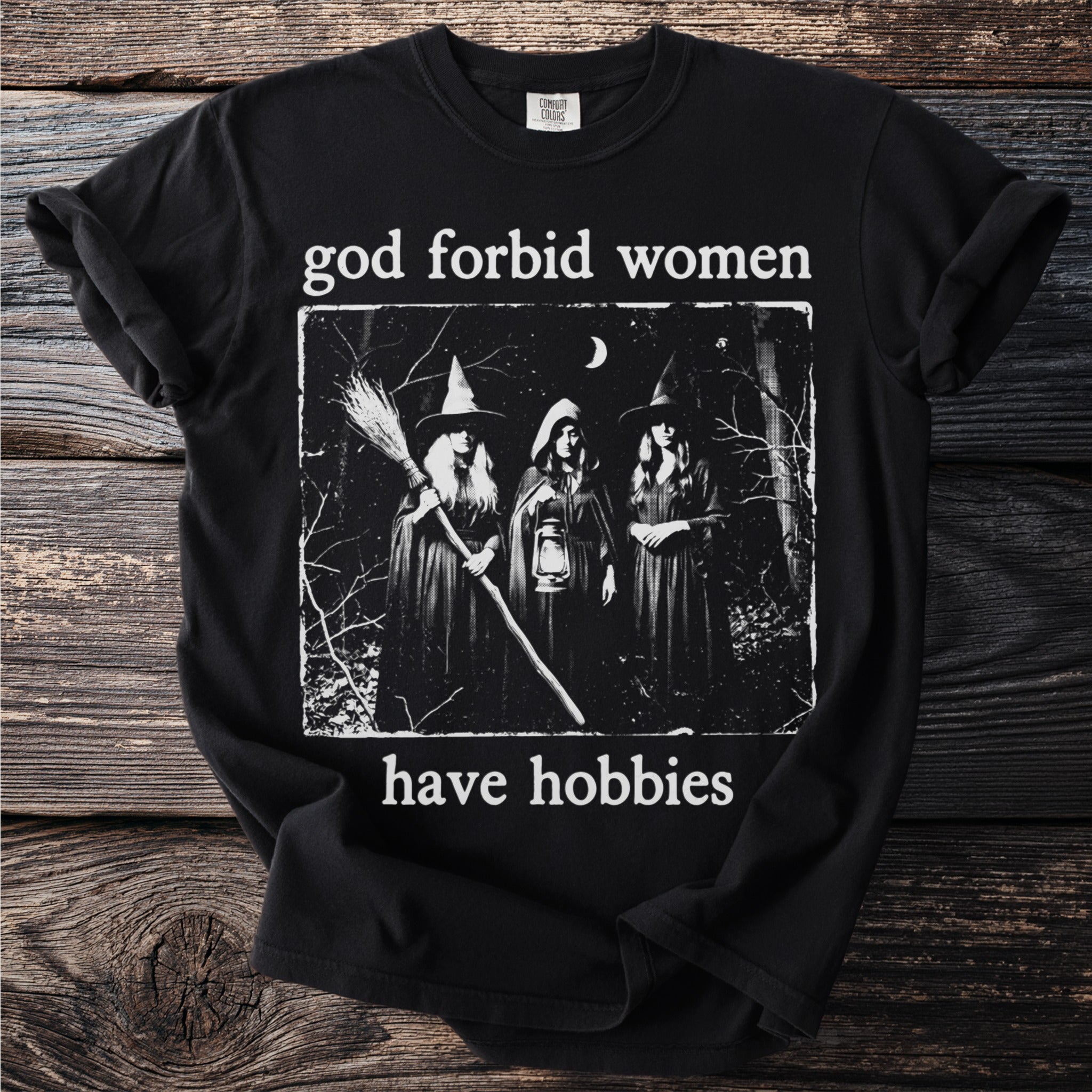 Black t-shirt with "god forbid women have hobbies" text and three witch illustration.