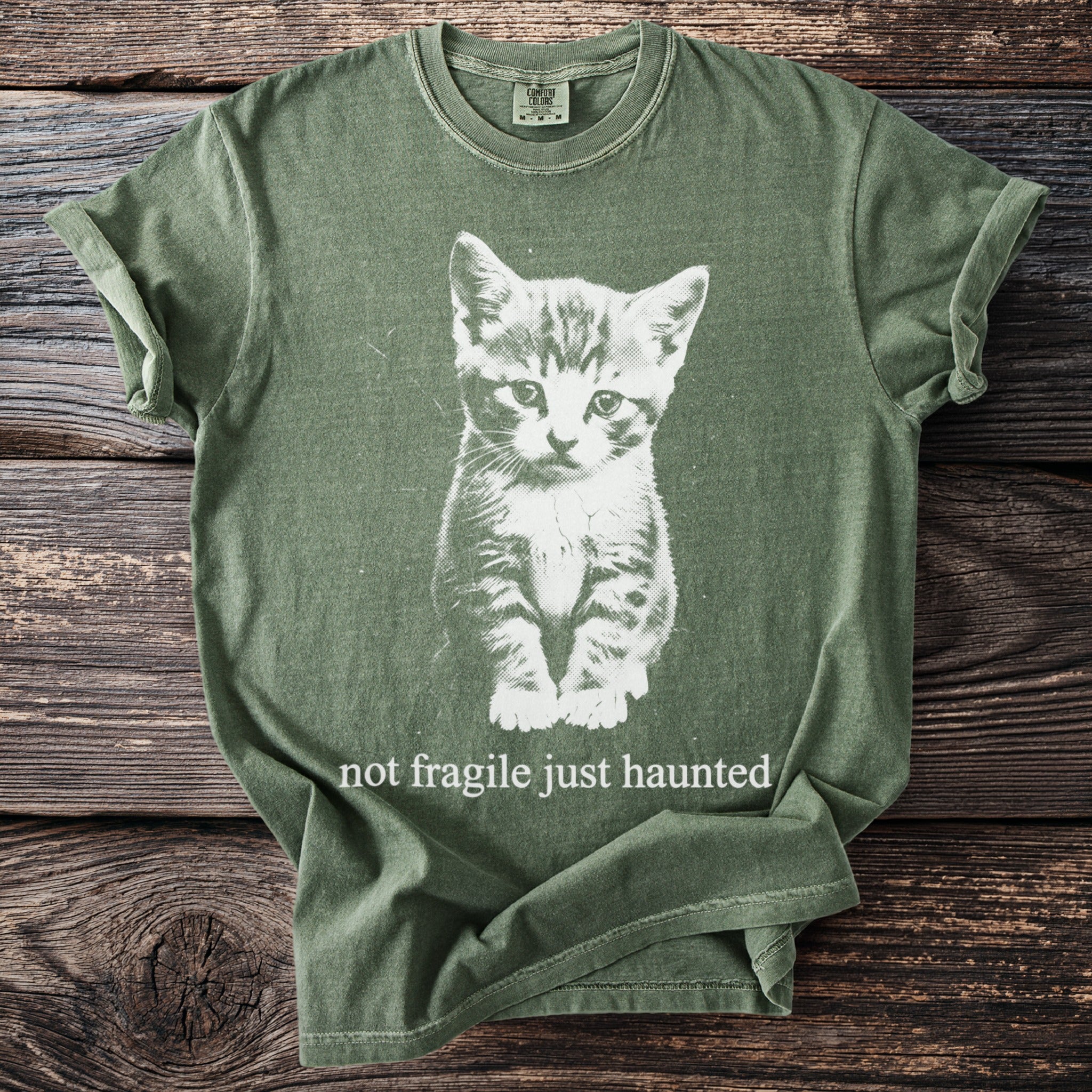 Green t-shirt with white graphic of a kitten and text "not fragile just haunted."