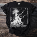 Black t-shirt with Bigfoot roasting a hot dog over a campfire graphic.
