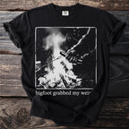 Black t-shirt with Bigfoot roasting a hot dog over a campfire graphic.