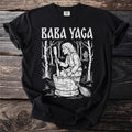 Black t-shirt with white Baba Yaga graphic featuring witch in barrel with broom and hut.