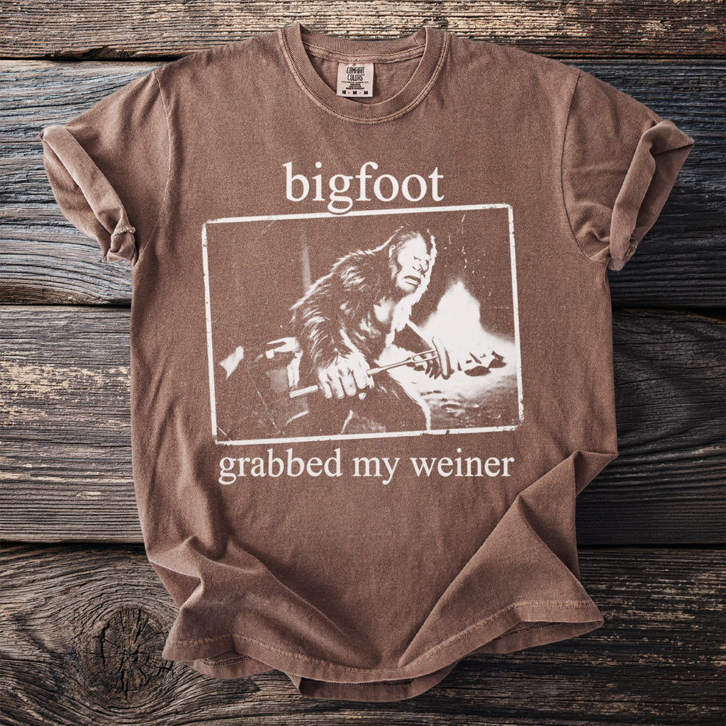 Brown t-shirt with white text and graphics of Bigfoot grabbing a stick.