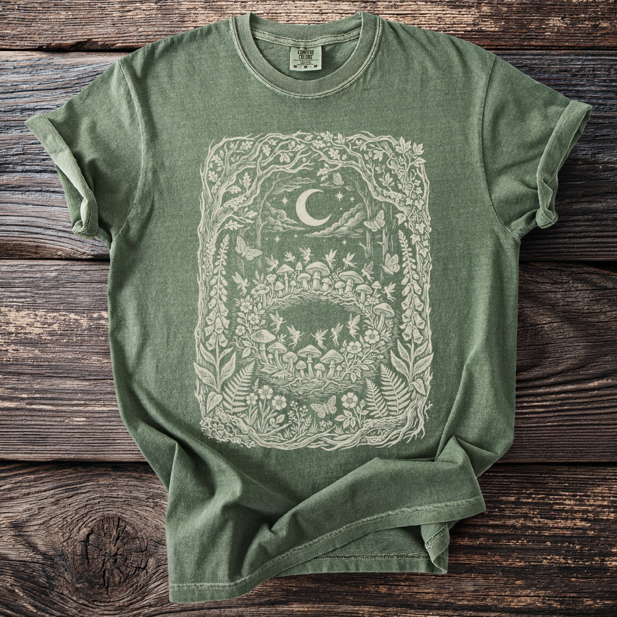 Green t-shirt with cream nature graphic of fairies, mushrooms, and a moon.