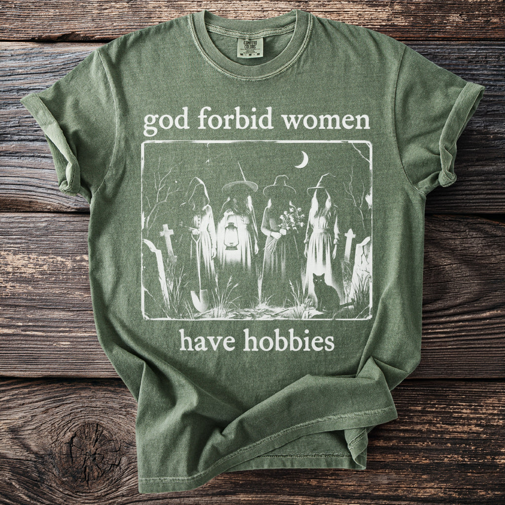 Green t-shirt with white graphic of four robed figures in a cemetery, a black cat, and text.