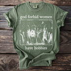 Green t-shirt with white graphic of four robed figures in a cemetery, a black cat, and text.