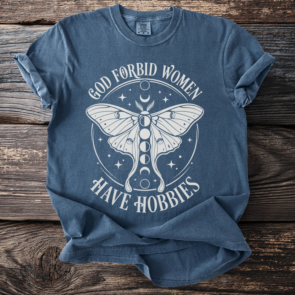 Blue t-shirt with white text and moth graphic that reads "God forbid women have hobbies".