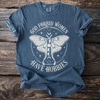 Blue t-shirt with white text and moth graphic that reads "God forbid women have hobbies".