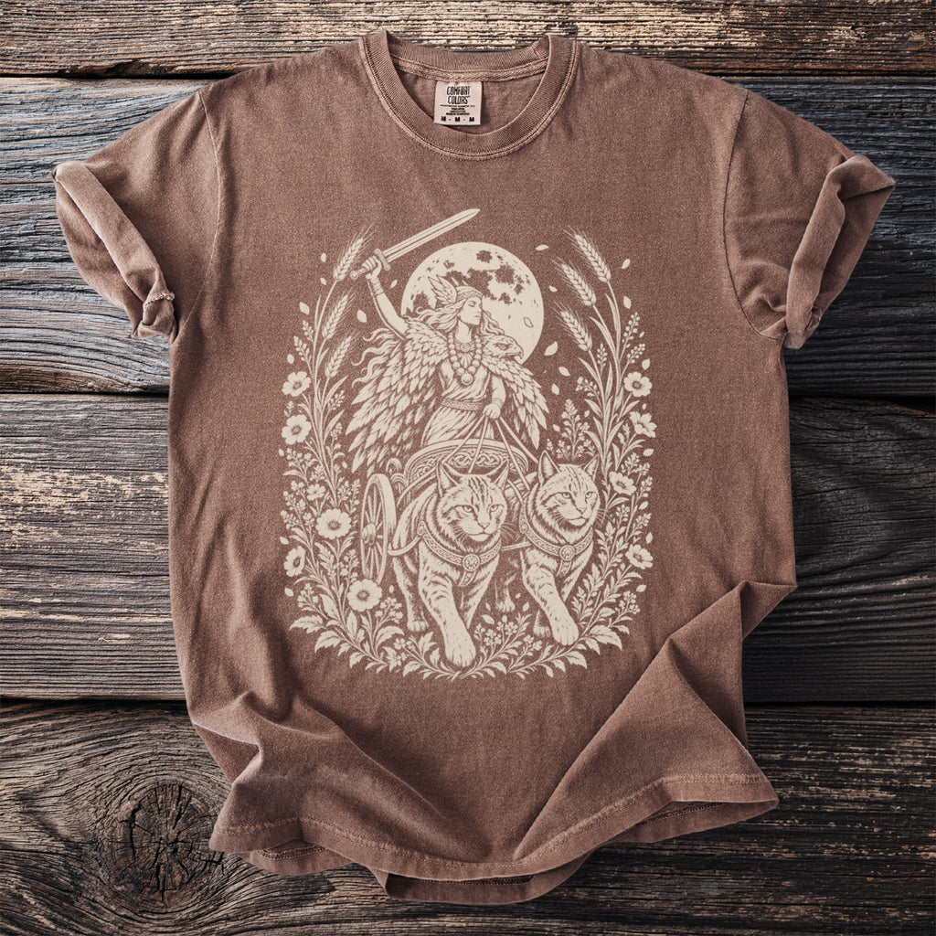 Brown t-shirt with a cream-colored illustration of a woman in a chariot pulled by two cats.