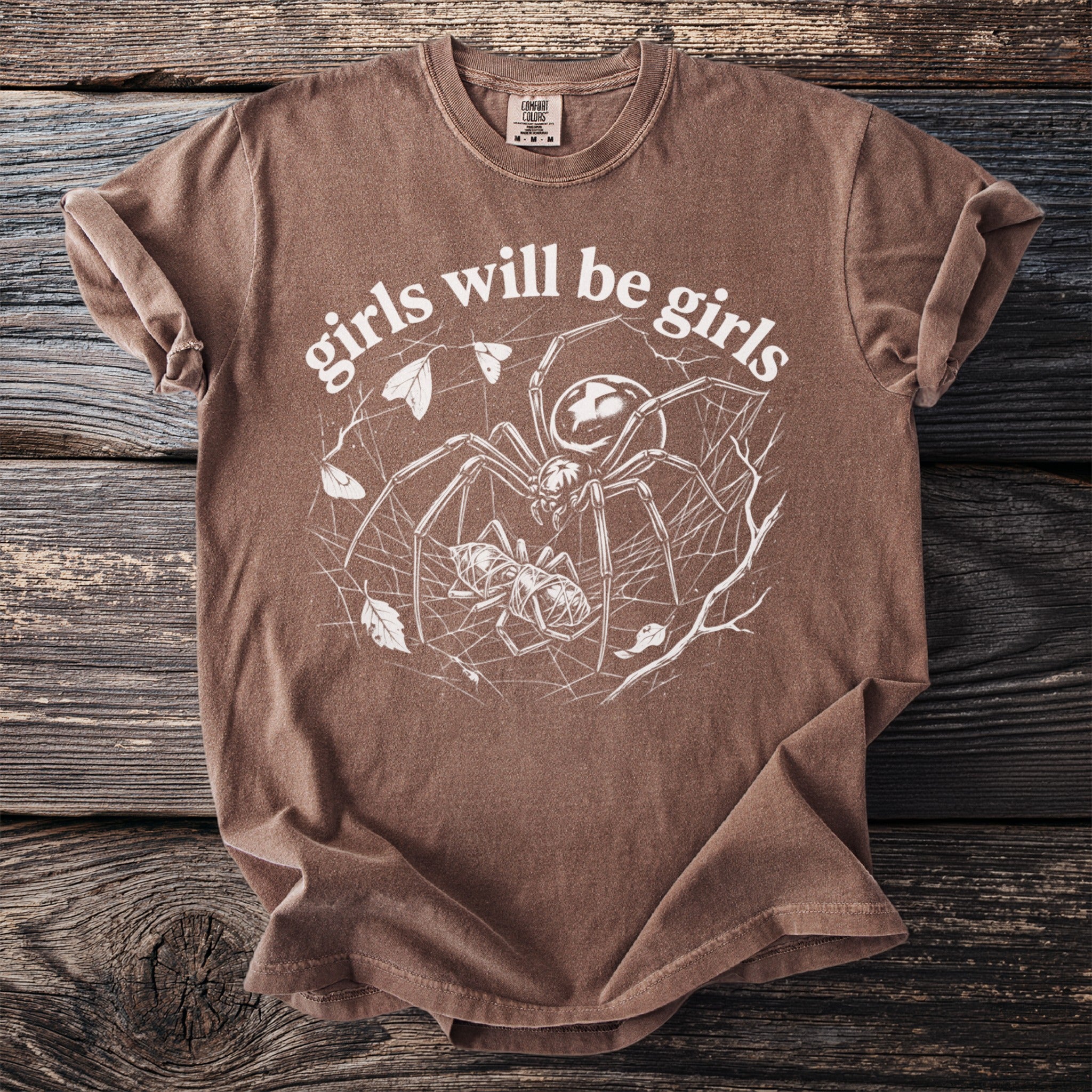 Brown t-shirt with white graphic of a spider, prey, and "girls will be girls" text.