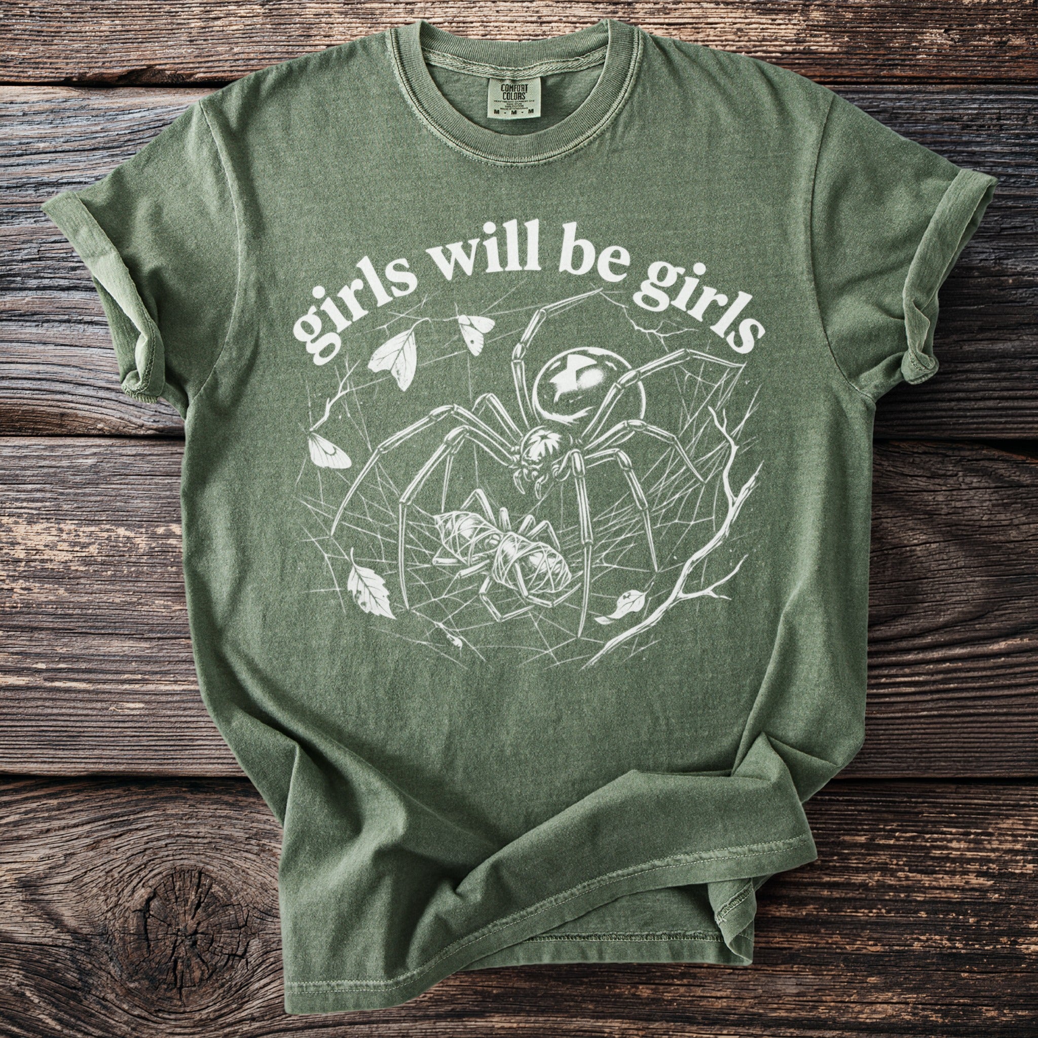 Green t-shirt with white graphic of a spider and prey, text reads "girls will be girls."