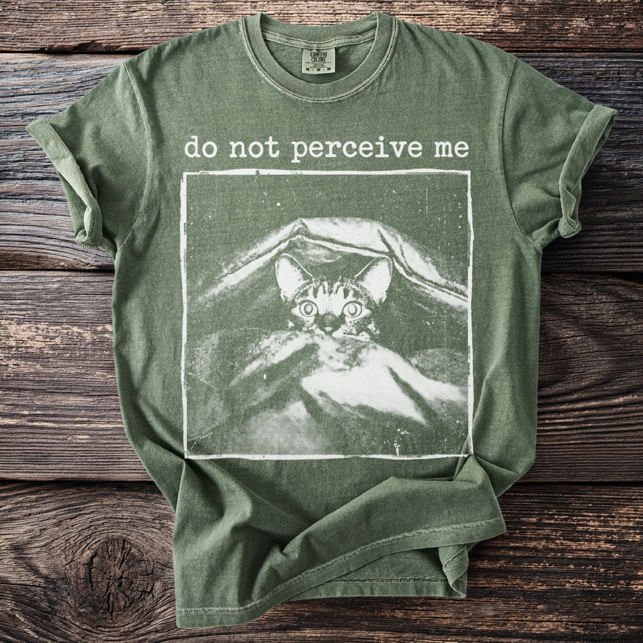 Green t-shirt with white text "do not perceive me" above a cat illustration.