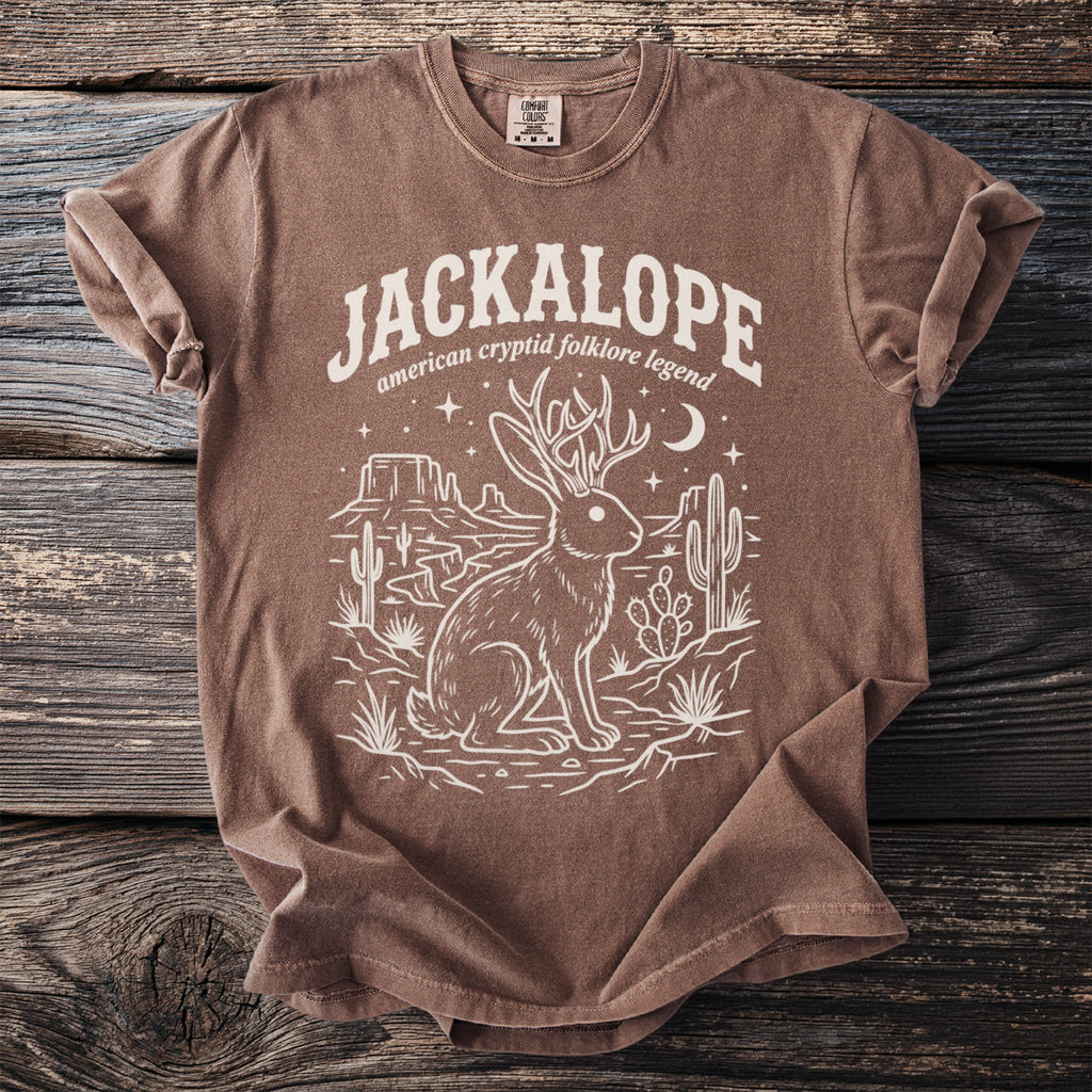 Brown t-shirt with a white graphic of a jackalope in a desert landscape.
