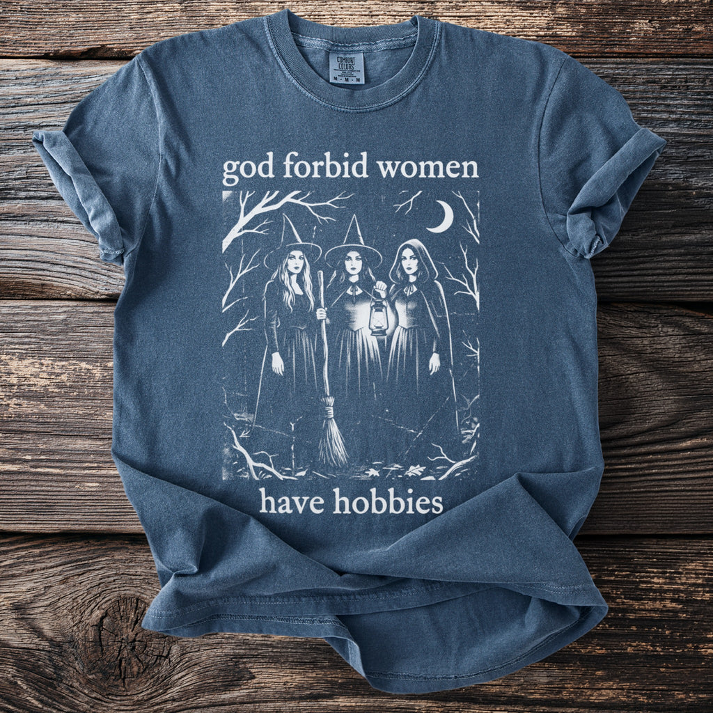 Blue t-shirt with witches, broom, lantern, moon, trees, and text "god forbid women have hobbies".