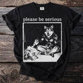 Black t-shirt with "please be serious" and a wolf illustration sitting and holding a can.