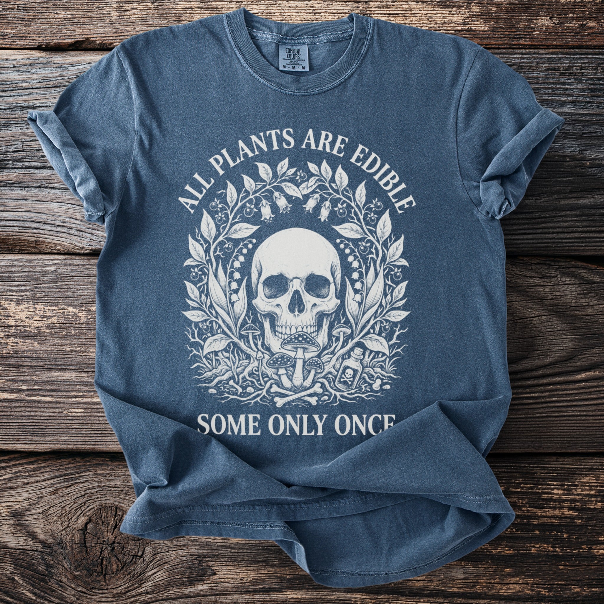 Blue t-shirt with skull and floral design, text reads "ALL PLANTS ARE EDIBLE SOME ONLY ONCE".