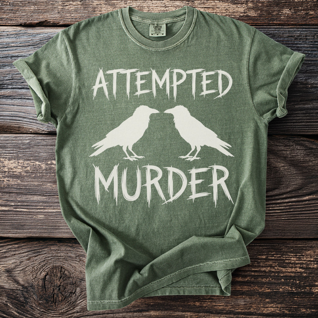 Green t-shirt with white text "ATTEMPTED MURDER" and two birds.