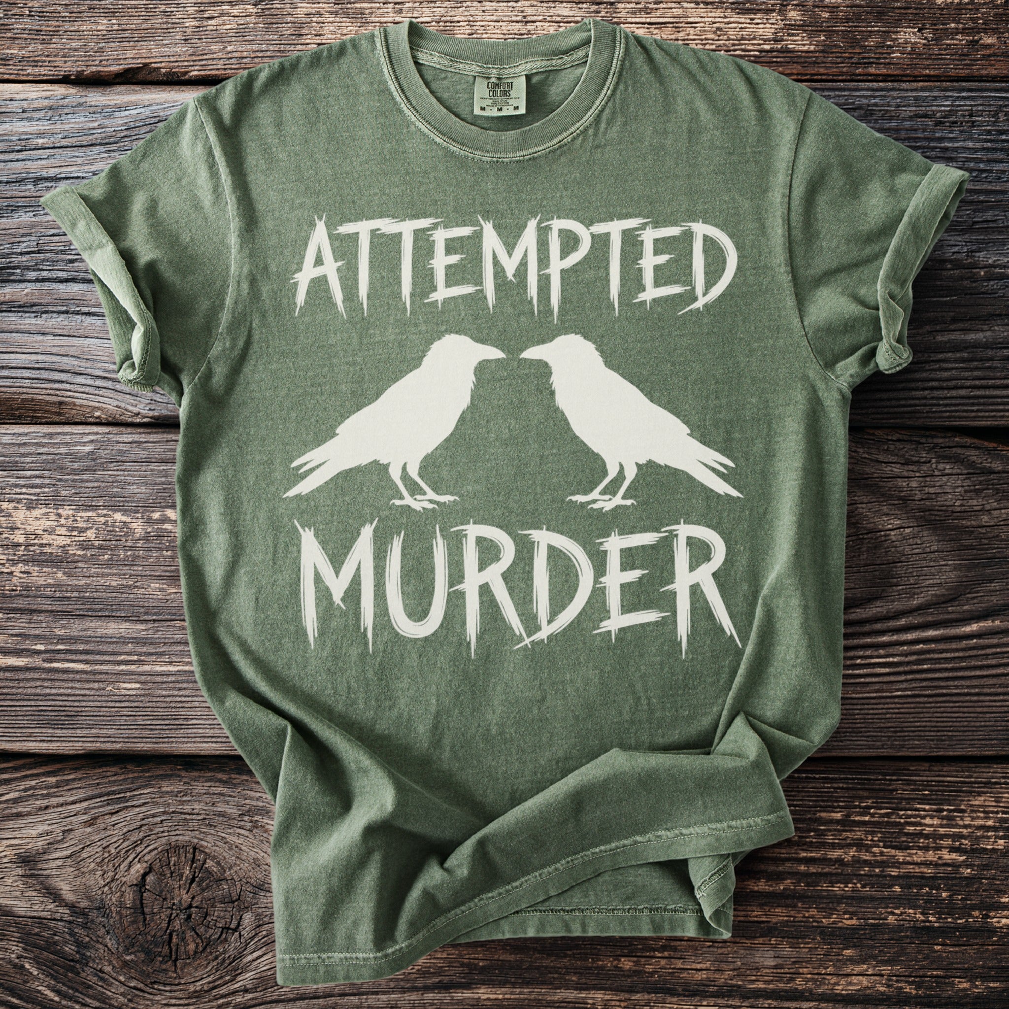 Green t-shirt with white text "ATTEMPTED MURDER" and two birds.