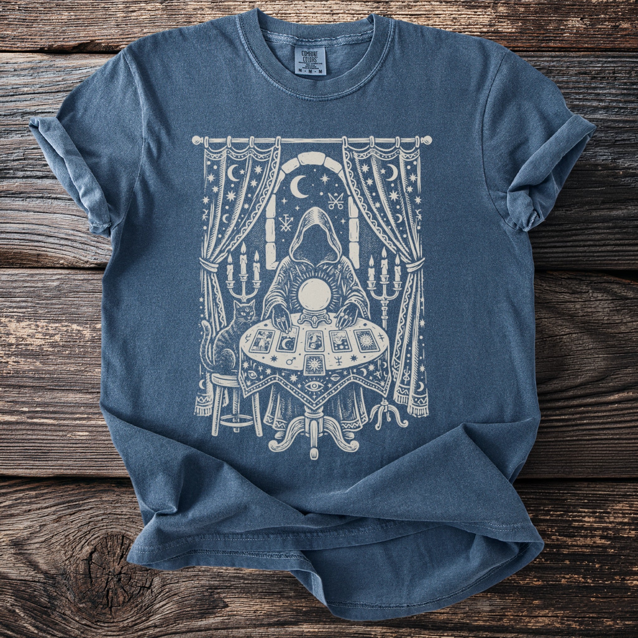 Blue t-shirt with white occult-themed graphic of a figure reading tarot cards and a crystal ball.