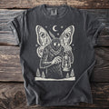 Pepper gray t-shirt with a cream folk-cut print: Mothman stands among snowy pines, lighting the wick of an old oil lantern.