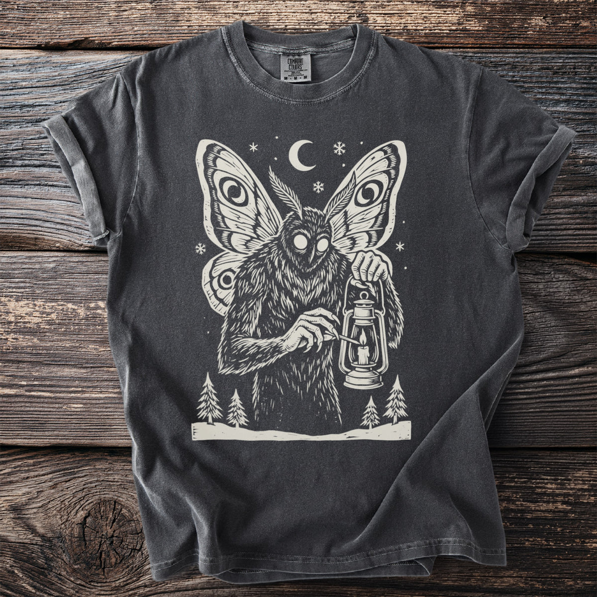 Pepper gray t-shirt with a cream folk-cut print: Mothman stands among snowy pines, lighting the wick of an old oil lantern.