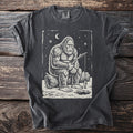 Pepper gray t-shirt with a cream folk-cut print: Bigfoot sits on a log with a stick rod over a hole in the ice, one small fish on the line.