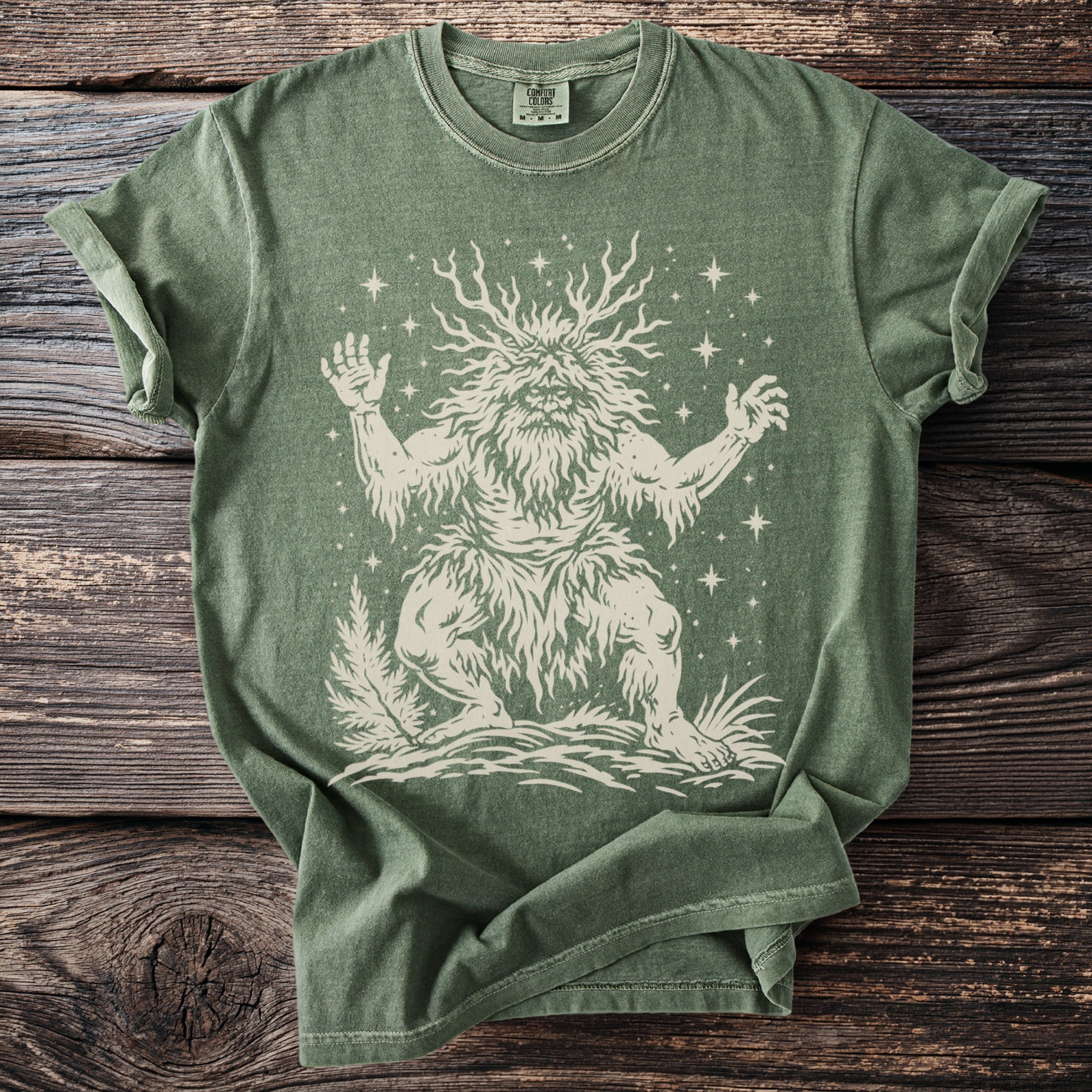 Green t-shirt with a cream graphic of a leafy, bearded creature with antlers and stars.