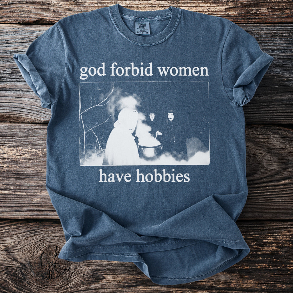 Blue t-shirt with white text "god forbid women have hobbies" and a graphic.