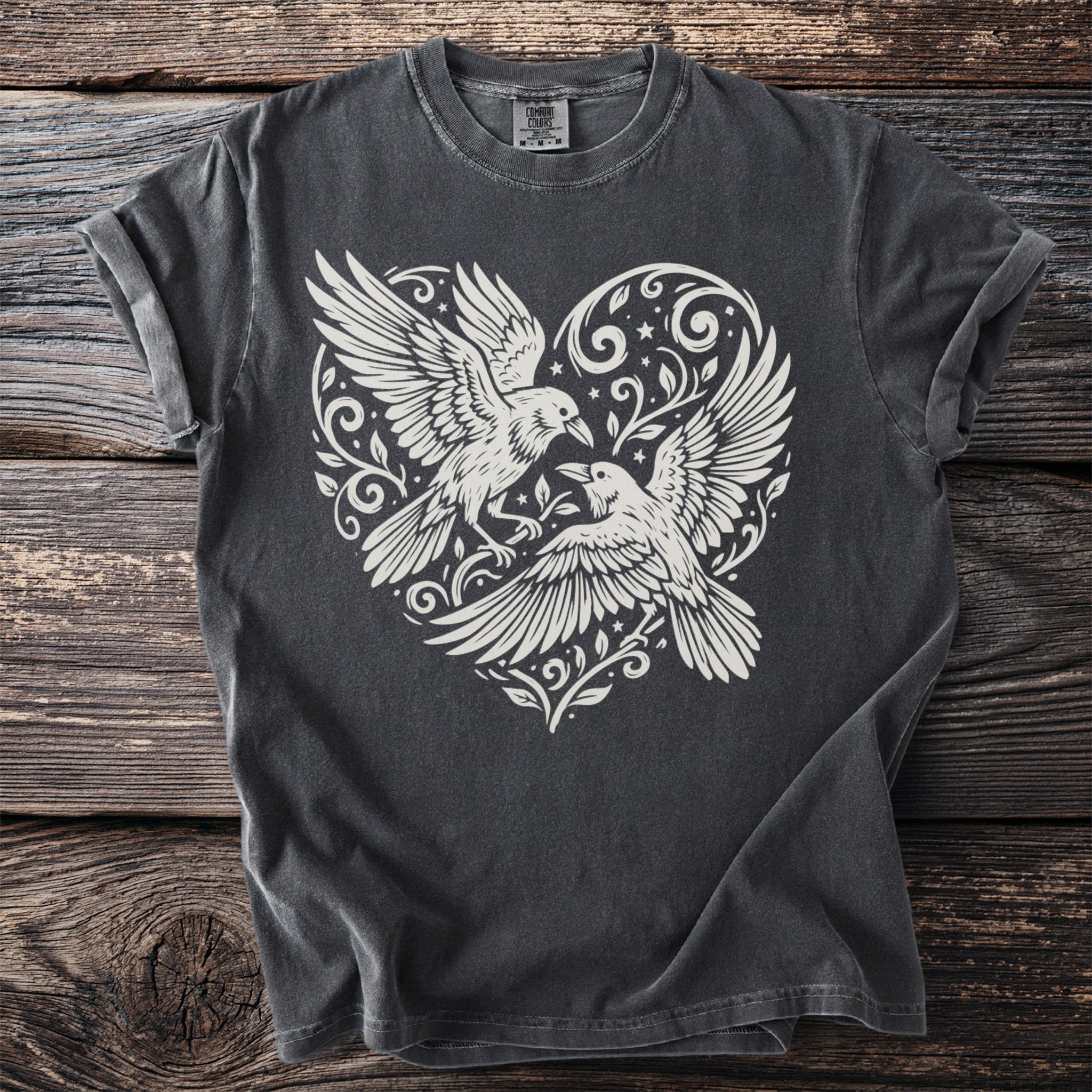 Dark t-shirt with white graphic of two birds in a heart with floral and star accents.
