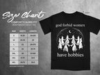 Black t-shirt with "god forbid women have hobbies" text and witch graphic, features size chart on left.