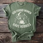 Green t-shirt with white text and graphic of three cats around a cauldron.