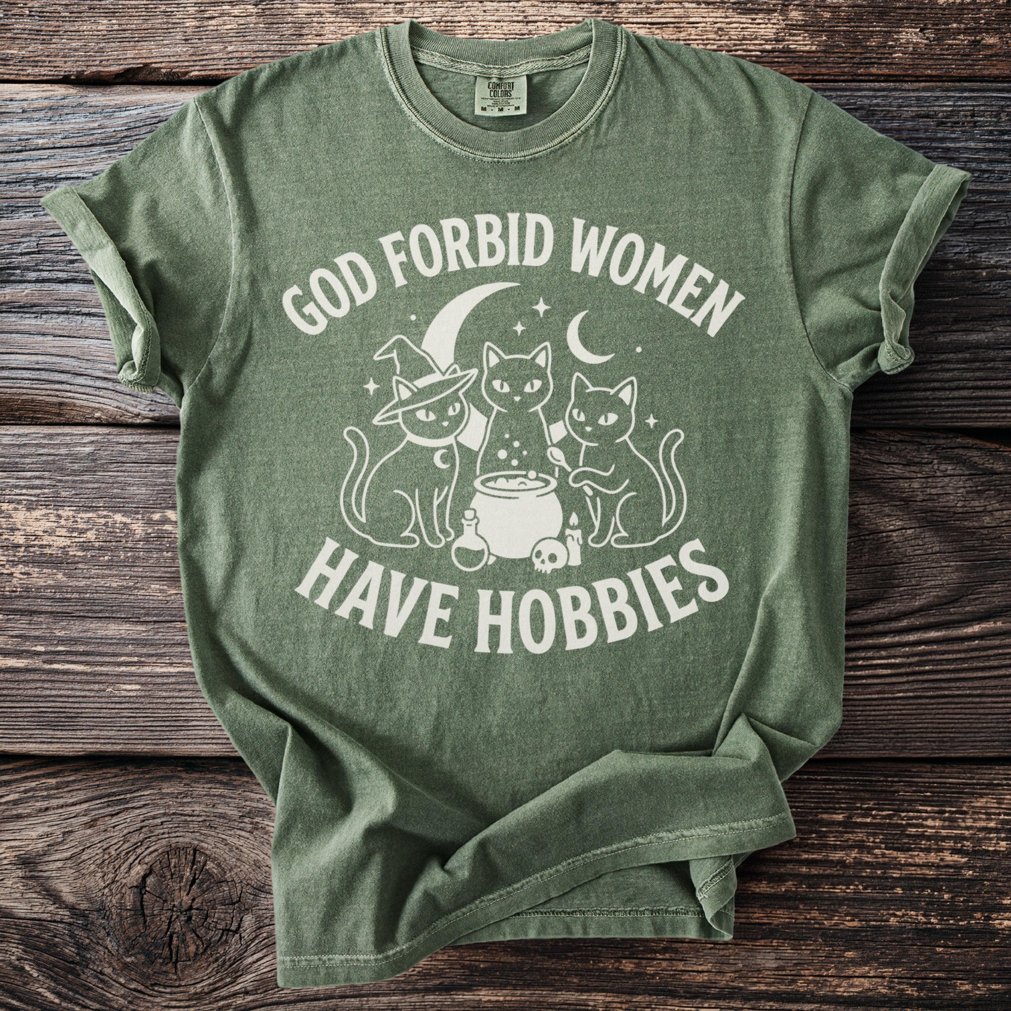 Green t-shirt with white text and graphic of three cats around a cauldron.