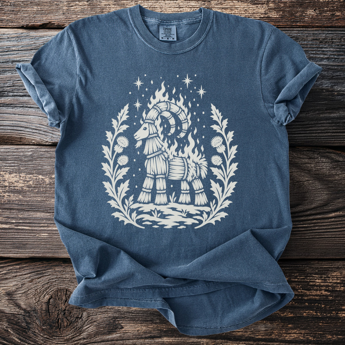 Blue t-shirt with a straw goat on fire, surrounded by thistles and stars.