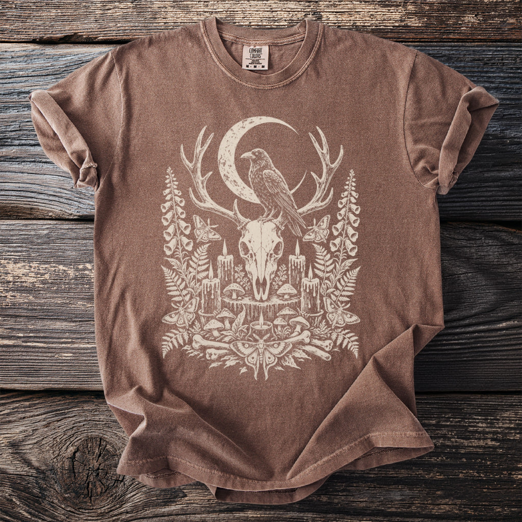 Brown t-shirt with a deer skull, raven, moon, candles, and nature design.