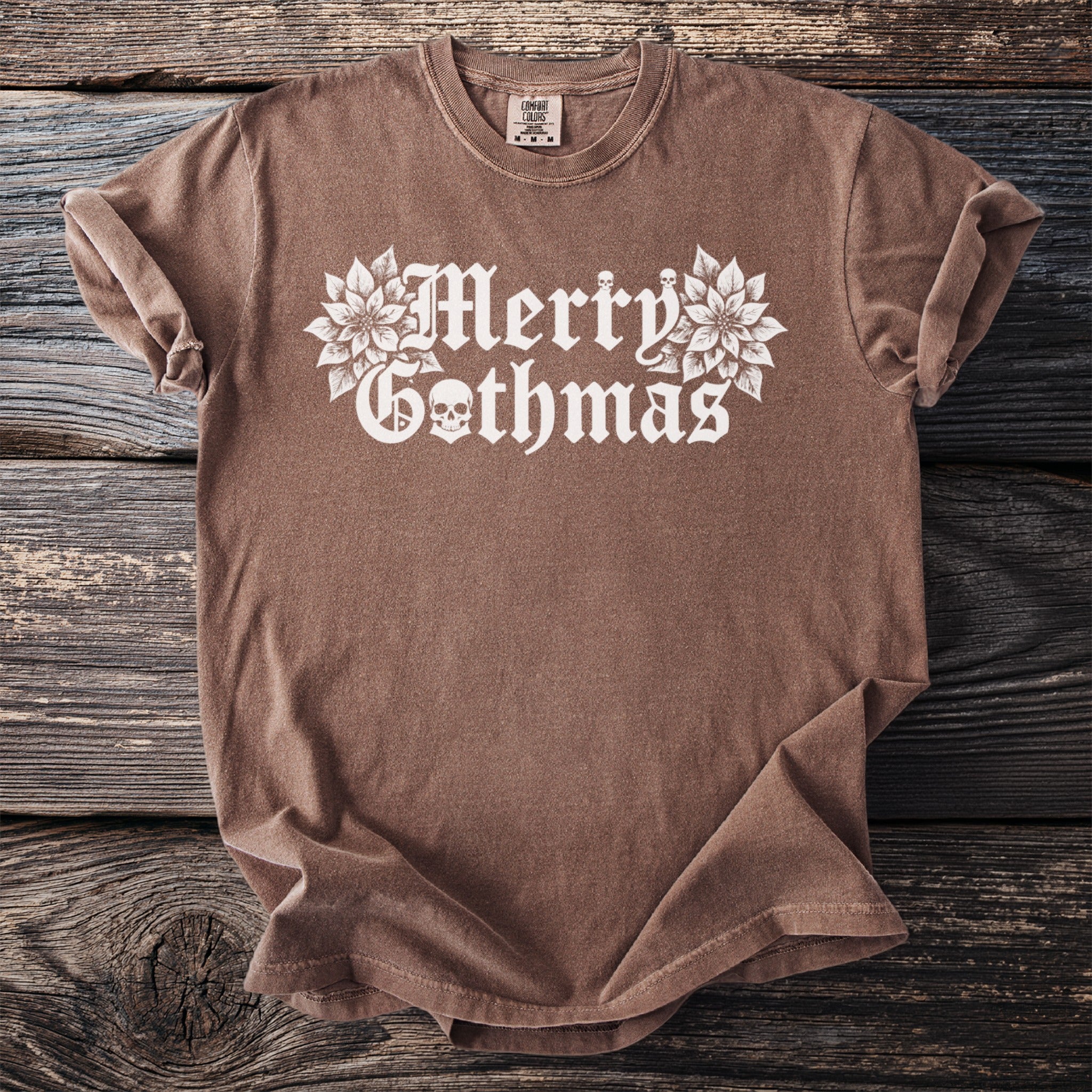 Brown t-shirt with white gothic text "Merry Gothmas" and floral skull graphic.