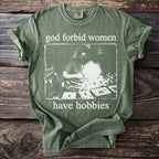 Green t-shirt with white text "god forbid women have hobbies" and a vintage graphic.