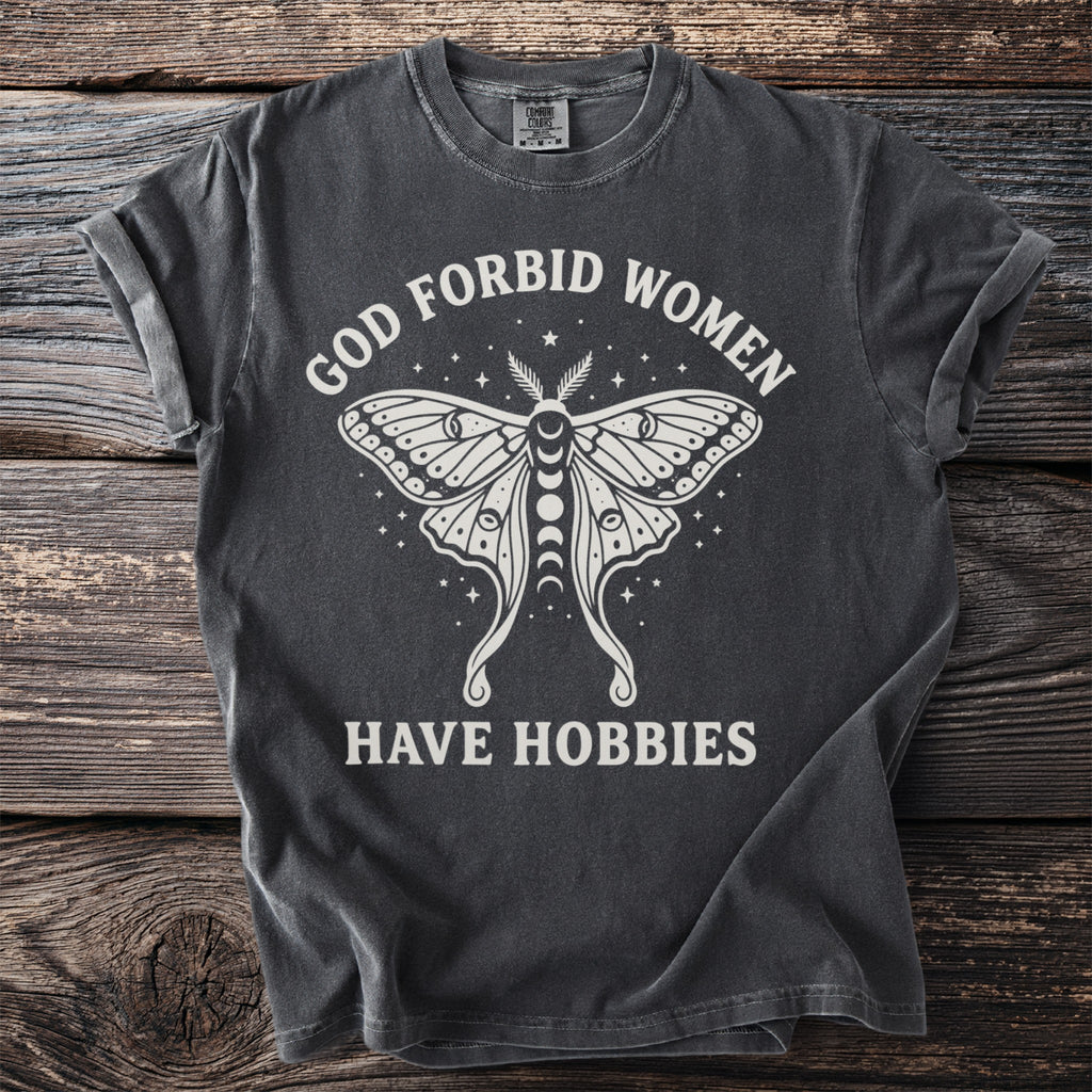 Dark gray t-shirt with white graphic and text: "GOD FORBID WOMEN HAVE HOBBIES".