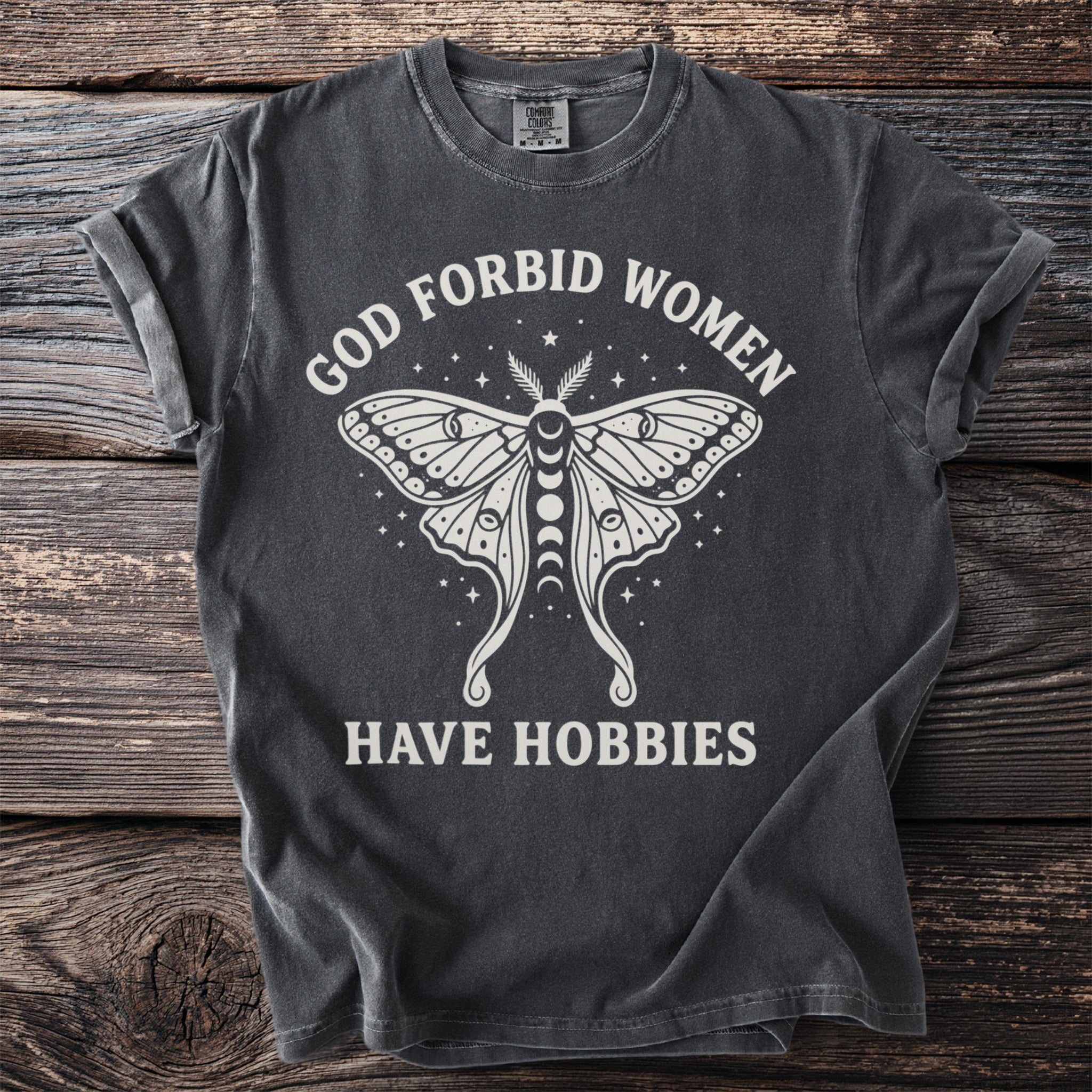 Dark gray t-shirt with white graphic and text: "GOD FORBID WOMEN HAVE HOBBIES".