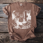 Brown t-shirt with white graphic of a cat on a bed, moth, spider, and text "you're not alone there are bugs".