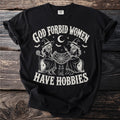 Black t-shirt with graphic of two skeleton witches holding a spiderweb, text reads "God Forbid Women Have Hobbies".