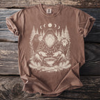 Brown t-shirt with a white graphic of a hooded figure with a beard, raven, wolf, trees, and moon phases.